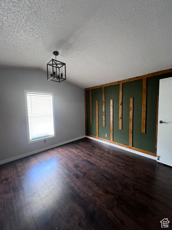 Spare room with vaulted ceiling, wood finished floors, a textured ceiling, baseboards, and a chandelier
