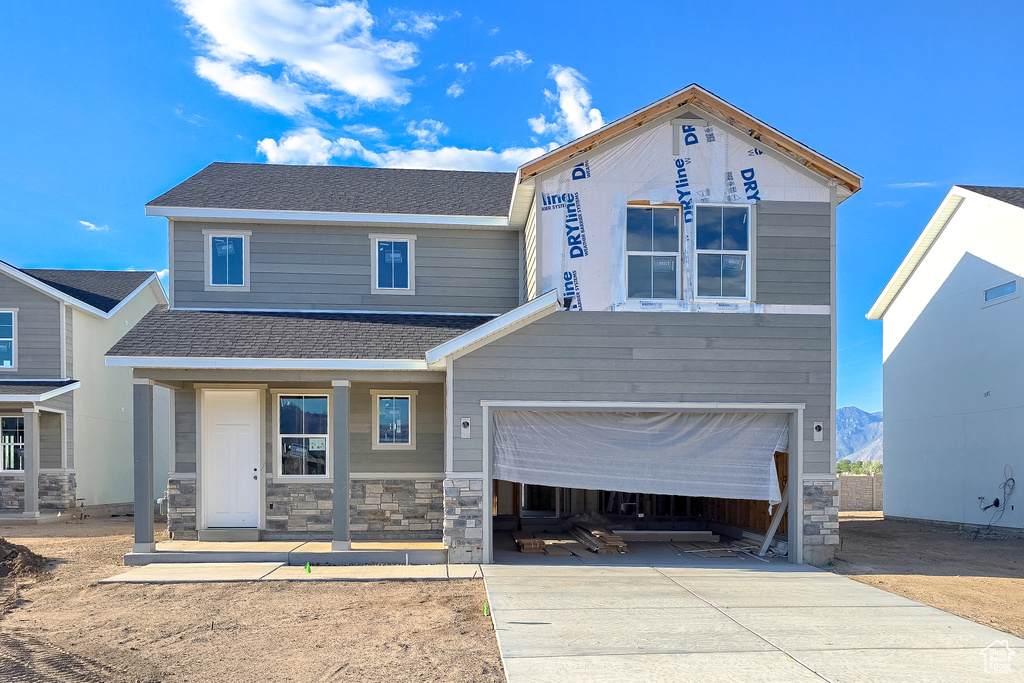 View of front of home with stone siding, concrete driveway, an attached garage, a shingled roof, and covered porch