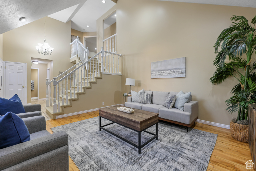 Living area featuring stairs, a chandelier, wood-type flooring, baseboards, and a high ceiling