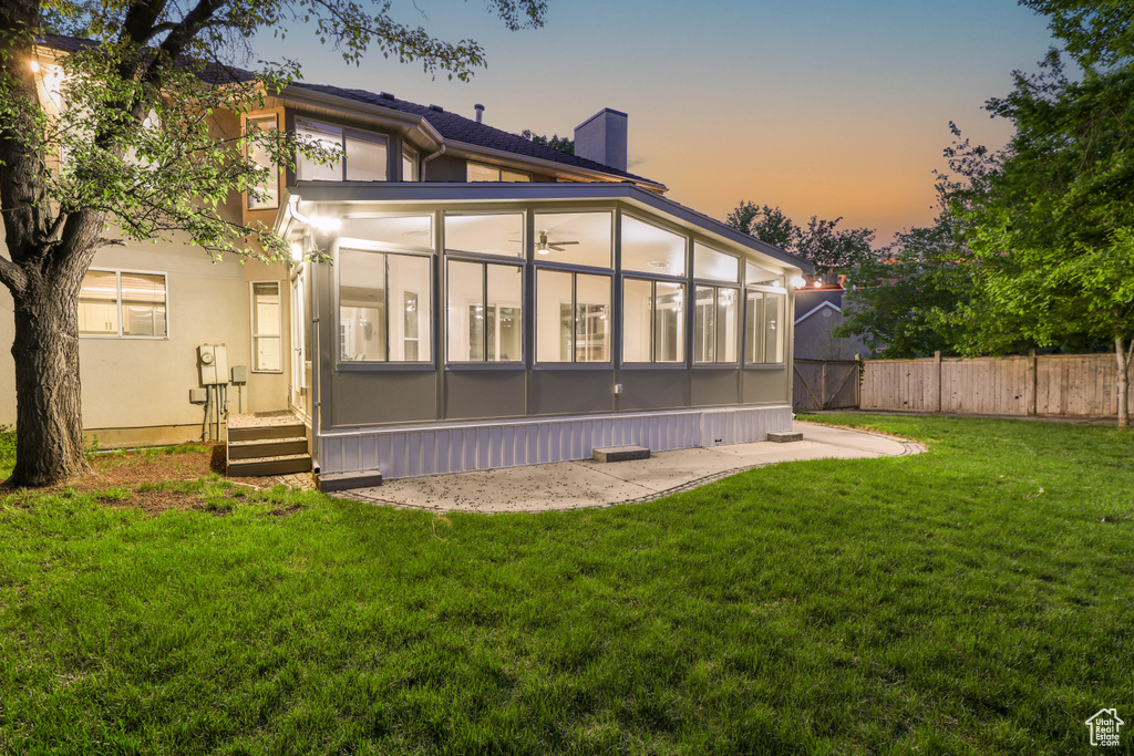 Back of property at dusk with a sunroom, a chimney, and stucco siding