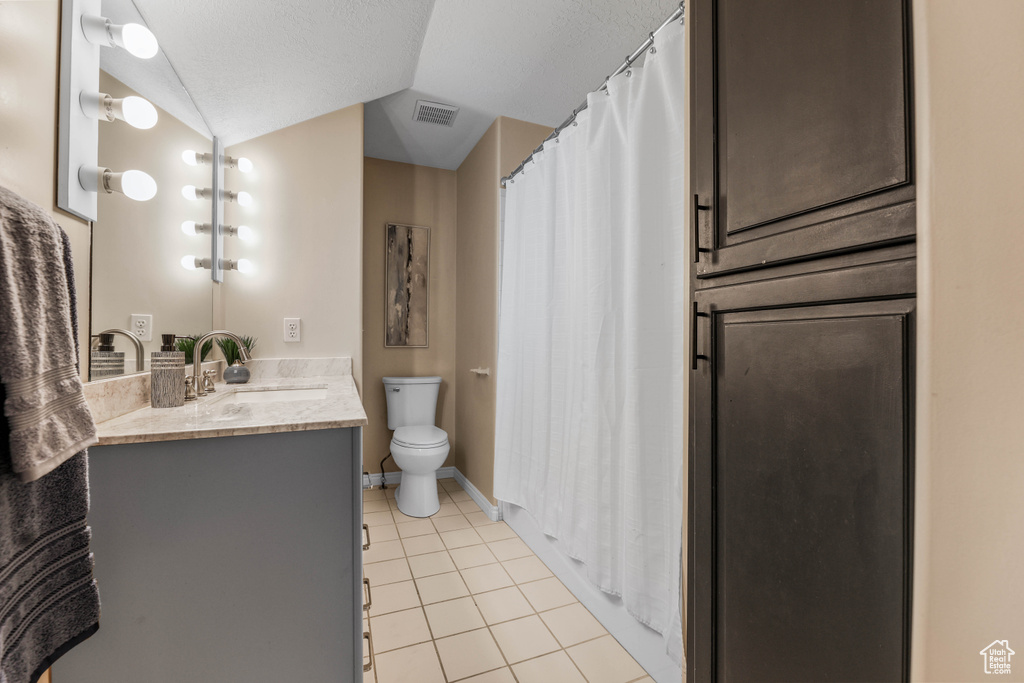 Bathroom featuring tile patterned flooring, toilet, vaulted ceiling, vanity, and baseboards