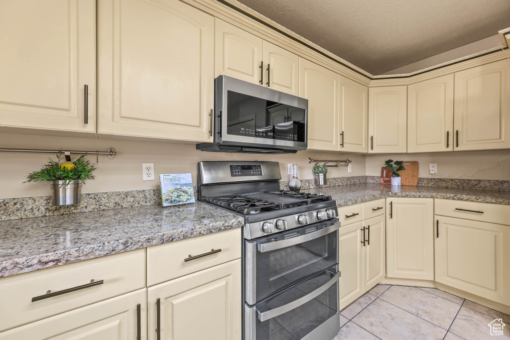 Kitchen featuring stainless steel appliances, cream cabinetry, light tile patterned floors, and light stone countertops