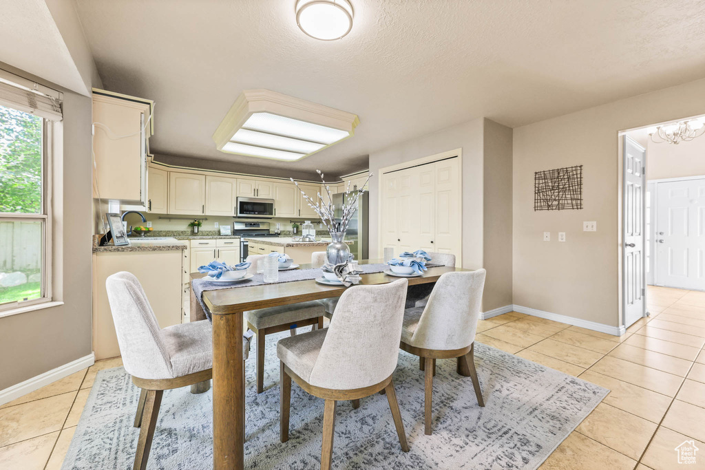 Dining area featuring light tile patterned flooring, baseboards, a chandelier, and a textured ceiling
