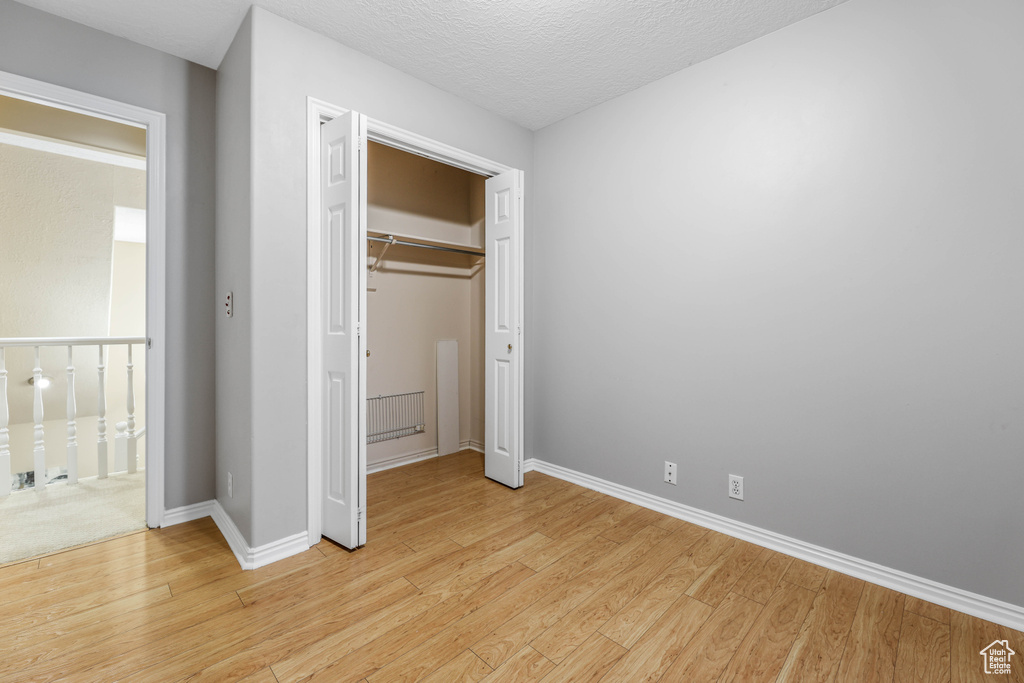 Unfurnished bedroom featuring light wood finished floors, baseboards, a closet, and a textured ceiling
