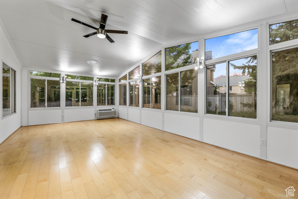 Unfurnished sunroom featuring wood finished floors, a wall mounted air conditioner, and vaulted ceiling