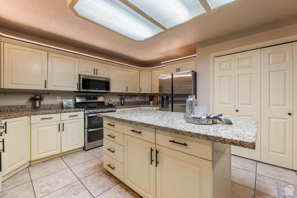Kitchen with appliances with stainless steel finishes, light tile patterned floors, cream cabinets, and light stone counters
