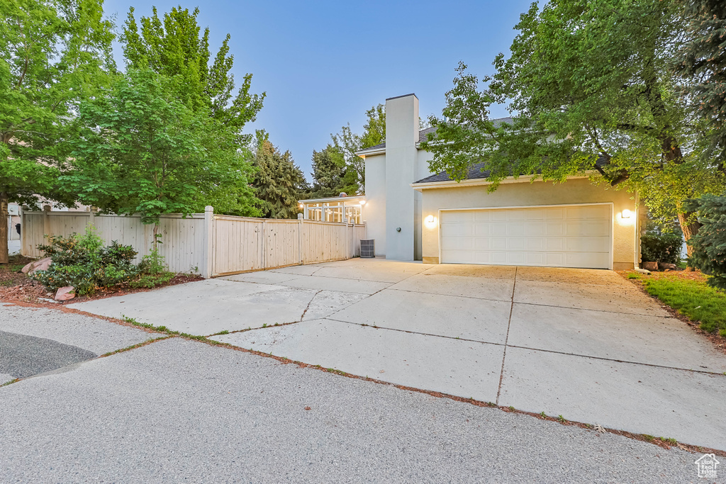 View of side of home featuring driveway, stucco siding, fence, a chimney, and central air condition unit