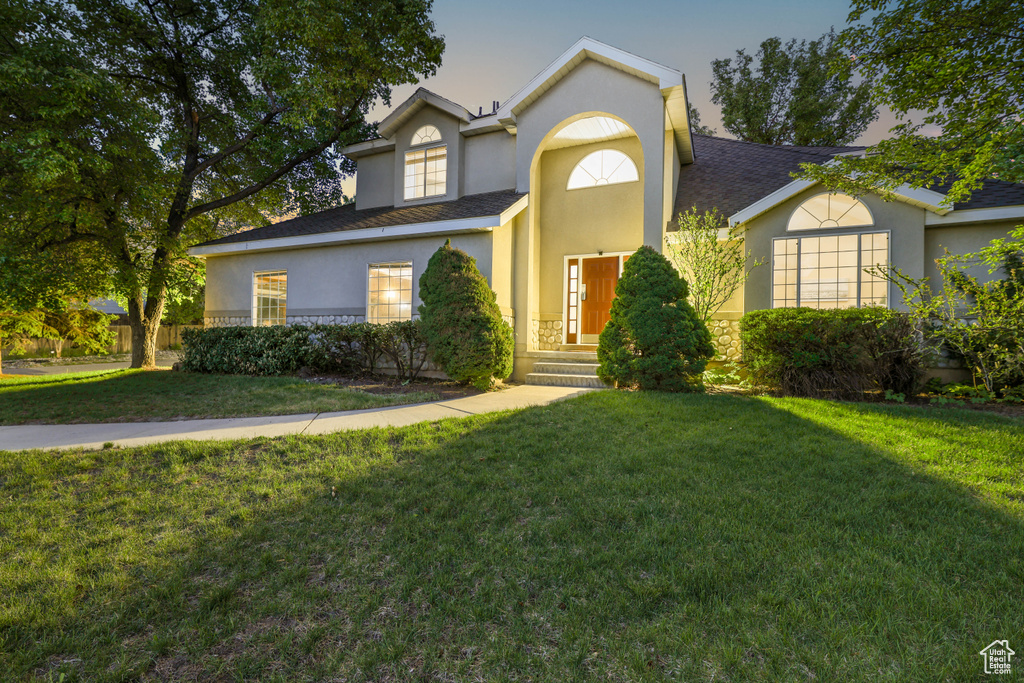 Traditional home featuring stucco siding, a front yard, and a shingled roof