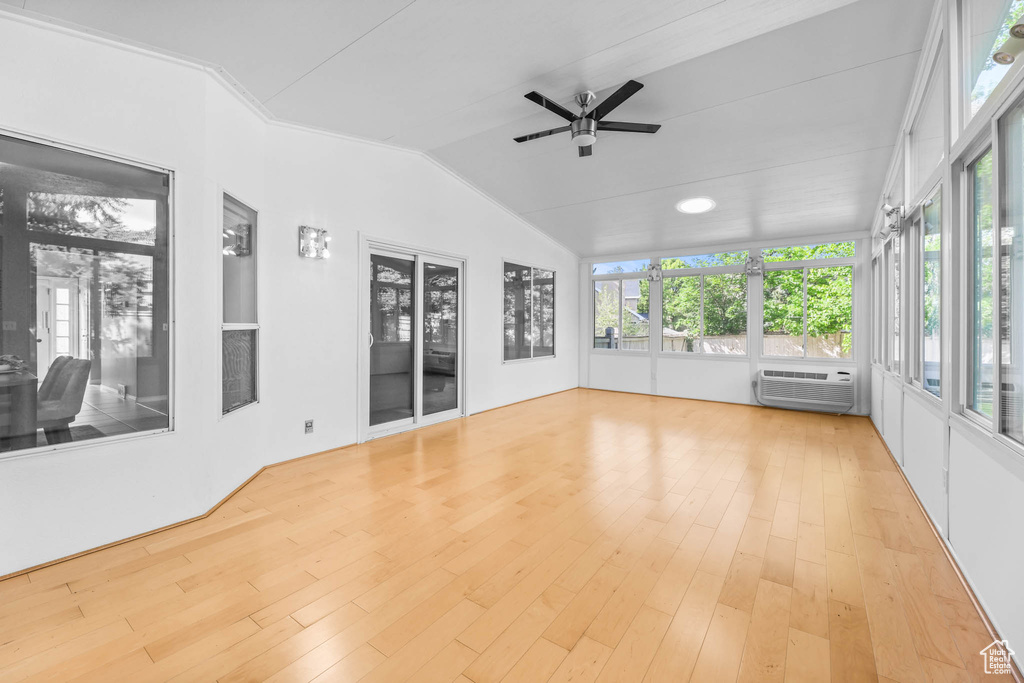 Unfurnished sunroom featuring lofted ceiling, wood finished floors, and a wall unit AC