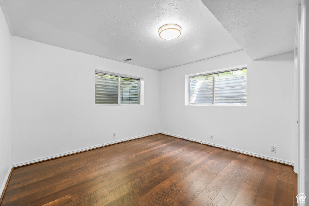 Empty room featuring dark wood-style flooring, baseboards, and a textured ceiling