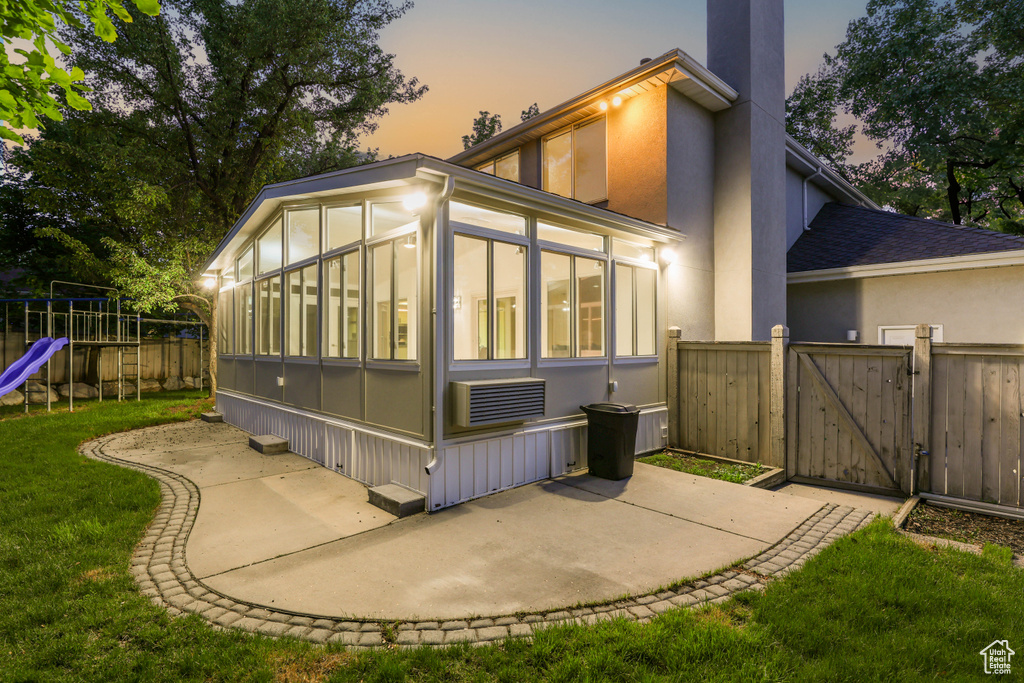 Back of house at dusk with a sunroom, a gate, a playground, a patio area, and stucco siding