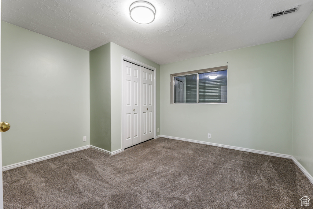 Unfurnished bedroom with carpet floors, baseboards, a closet, and a textured ceiling