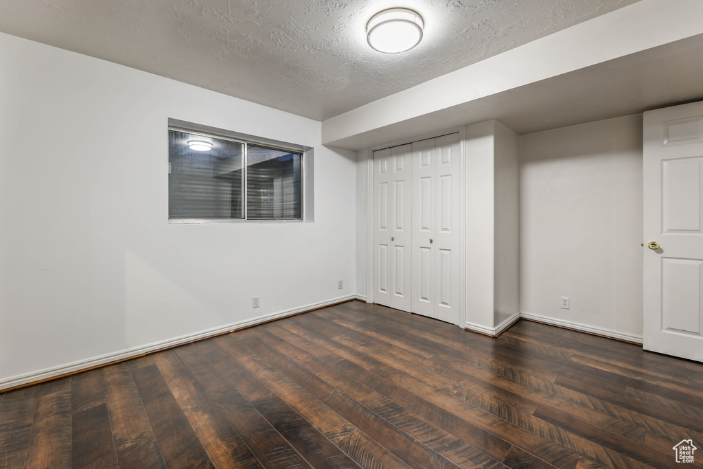 Unfurnished bedroom featuring dark wood finished floors, baseboards, a textured ceiling, and a closet