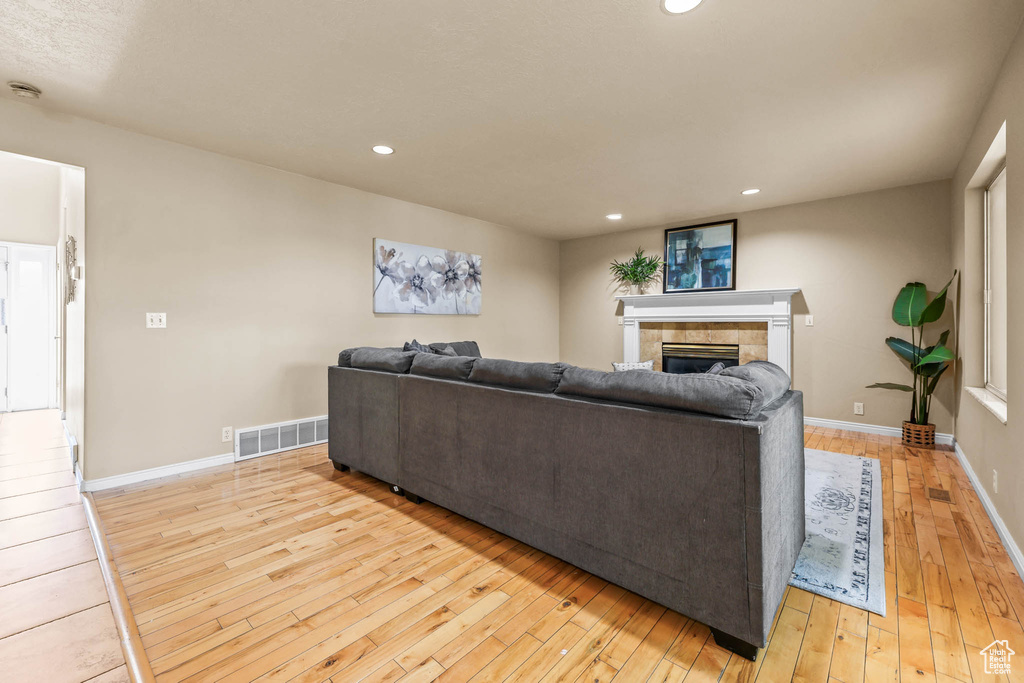 Living area with light wood-style floors, a tiled fireplace, baseboards, and recessed lighting
