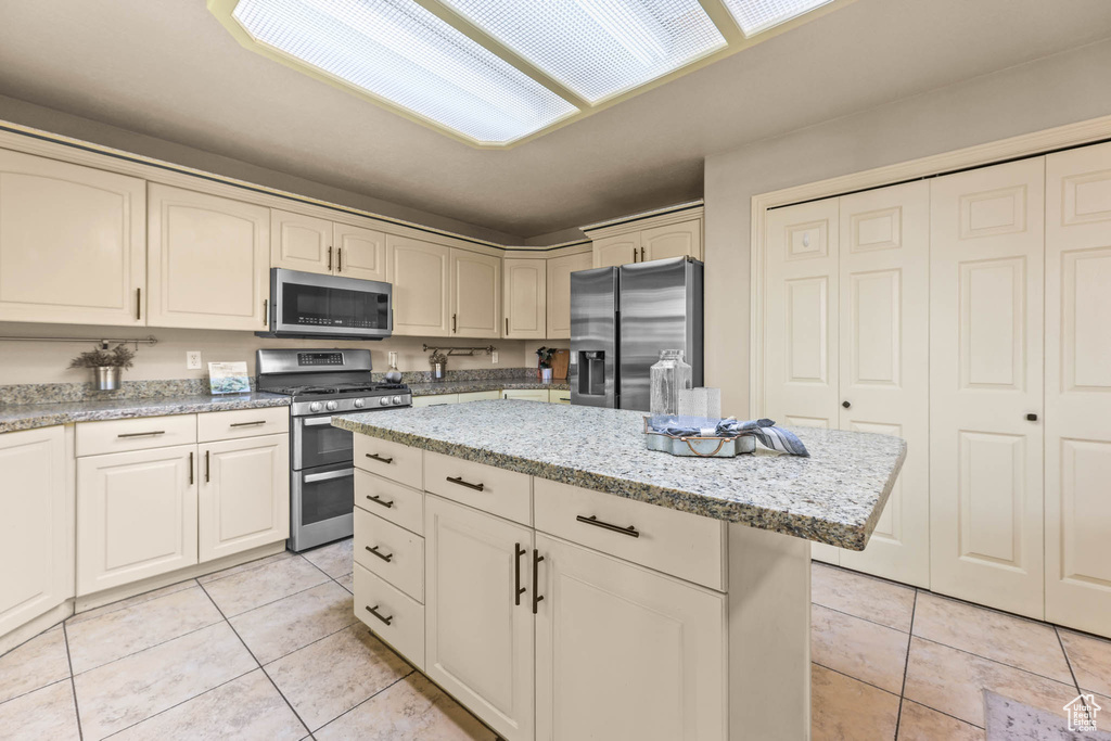 Kitchen featuring appliances with stainless steel finishes, light tile patterned floors, a center island, and light stone countertops