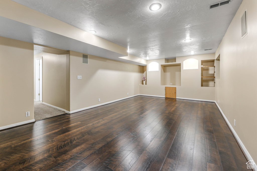 Finished below grade area with hardwood / wood-style flooring, a textured ceiling, and baseboards