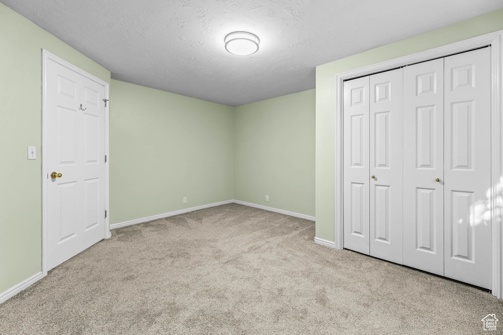 Unfurnished bedroom with carpet flooring, baseboards, a textured ceiling, and a closet