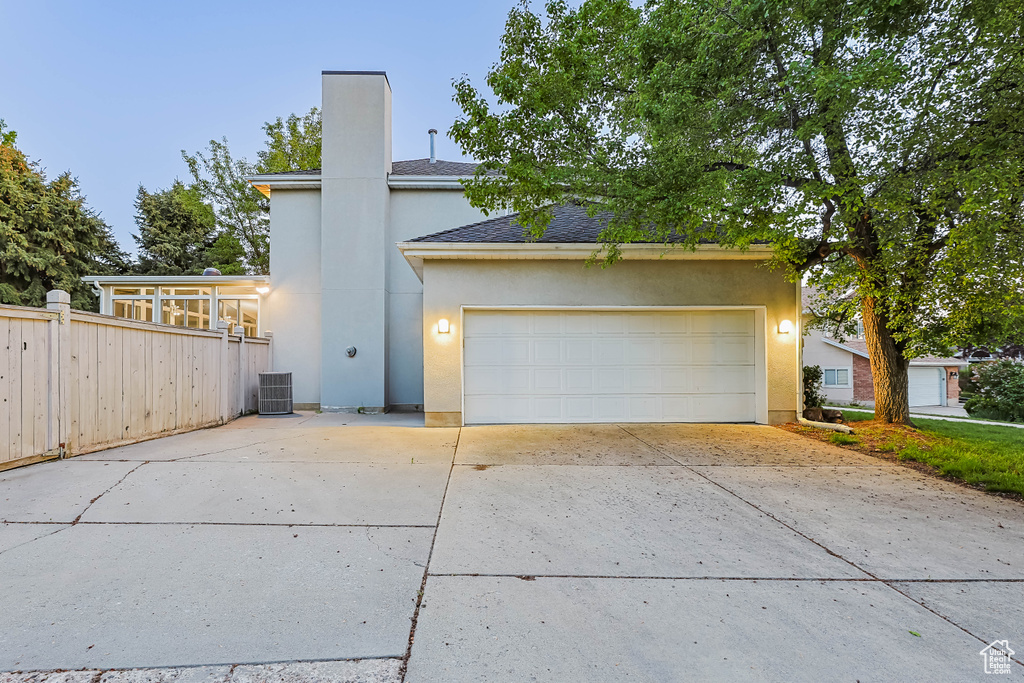 View of front facade with concrete driveway, stucco siding, central AC, a chimney, and fence