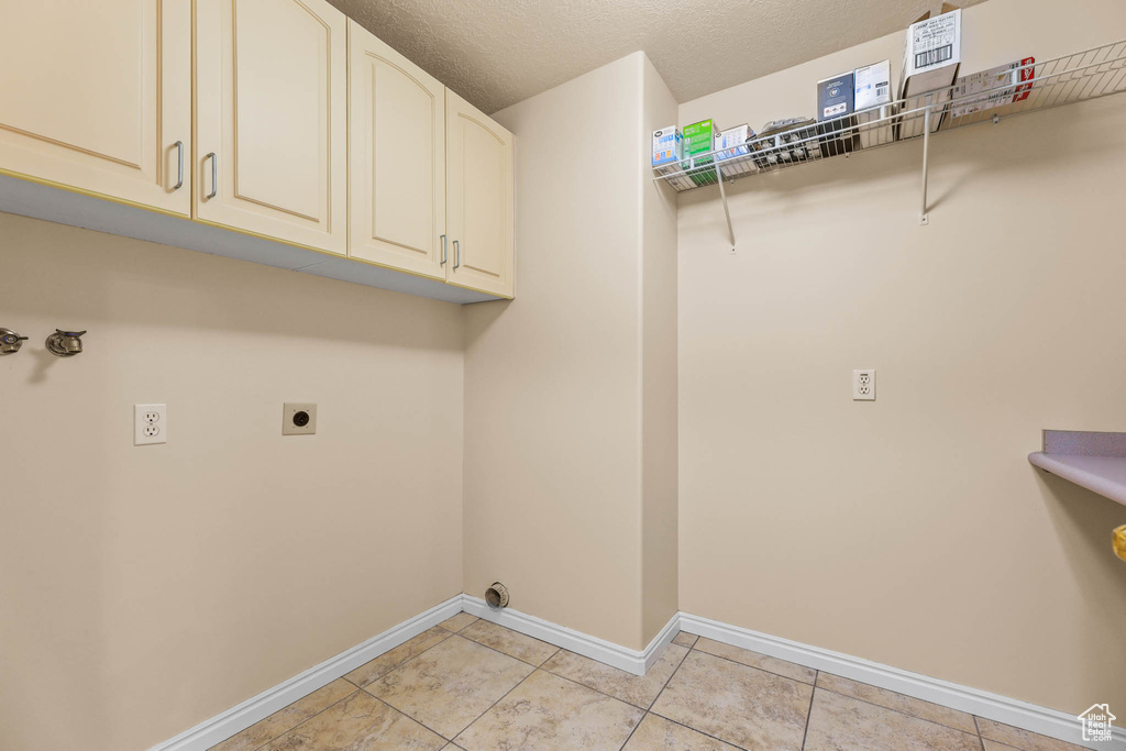 Washroom featuring electric dryer hookup, cabinet space, baseboards, light tile patterned floors, and a textured ceiling