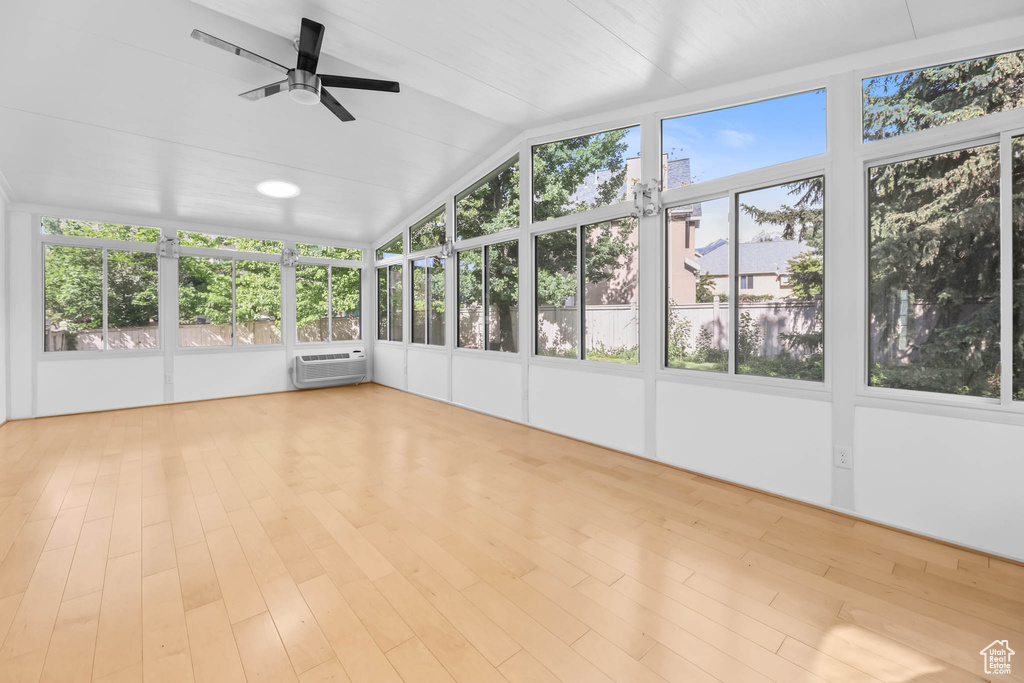 Unfurnished sunroom with ceiling fan, a wall mounted AC, lofted ceiling, and wood finished floors