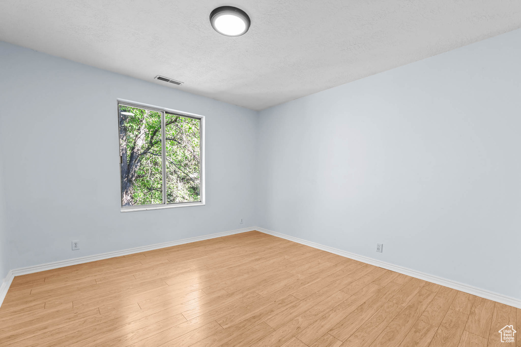 Spare room featuring light wood finished floors, baseboards, and a textured ceiling