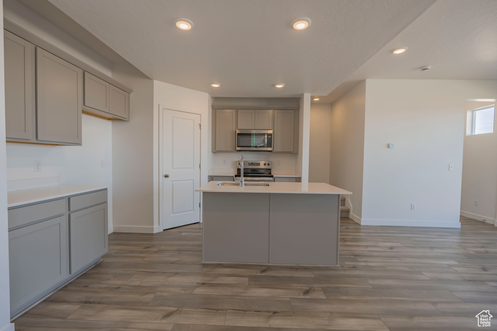 Kitchen with gray cabinetry, appliances with stainless steel finishes, baseboards, light wood-style flooring, and recessed lighting