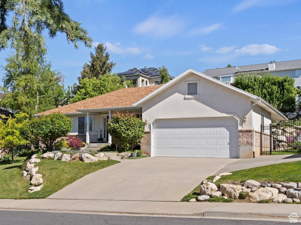View of front facade featuring an attached garage, concrete driveway, a front yard, brick siding, and a gate