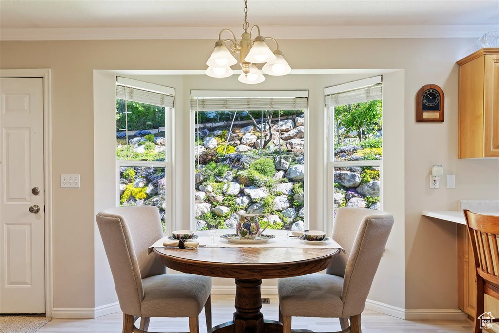 Dining room with a chandelier, baseboards, light wood-style flooring, and crown molding