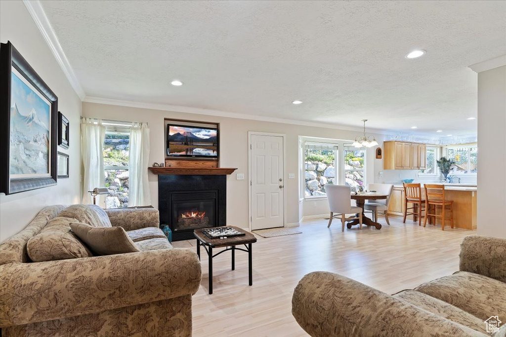 Living area with light wood-style floors, a glass covered fireplace, a chandelier, ornamental molding, and recessed lighting