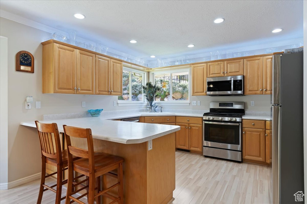 Kitchen featuring stainless steel appliances, a peninsula, a sink, light wood-style floors, and a breakfast bar