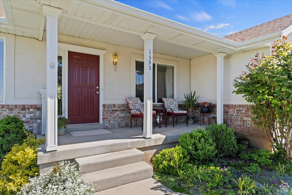 Property entrance with a porch, brick siding, and a shingled roof