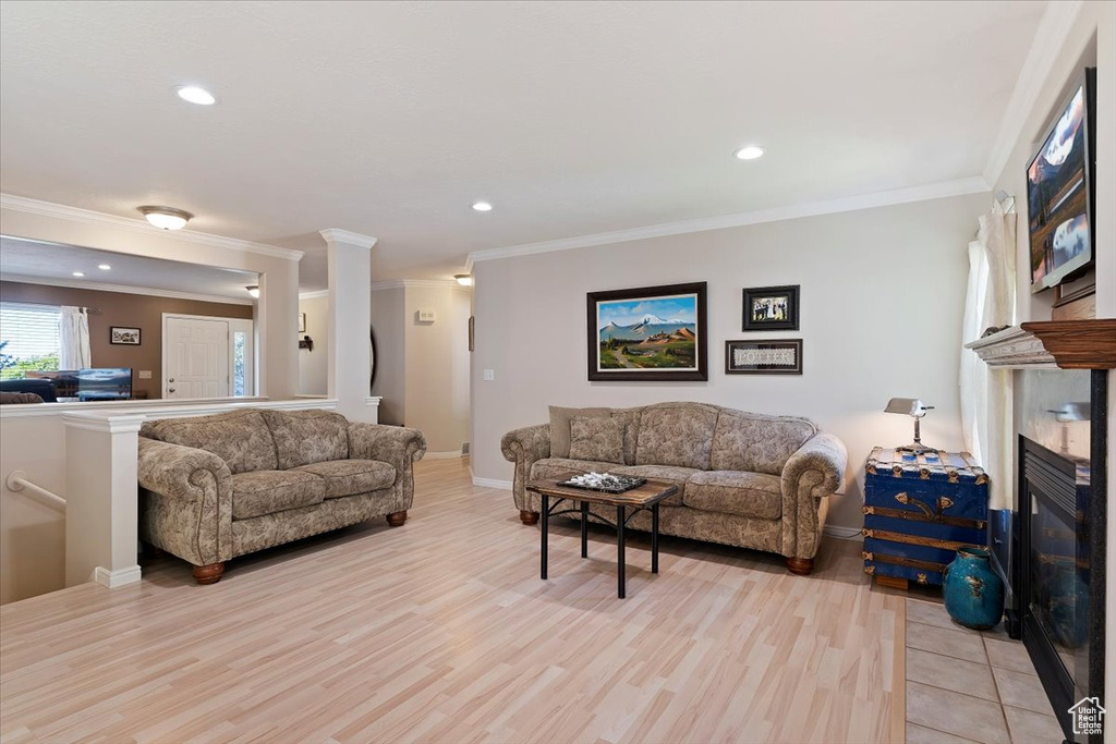 Living area featuring light wood-type flooring, baseboards, crown molding, recessed lighting, and a fireplace with flush hearth