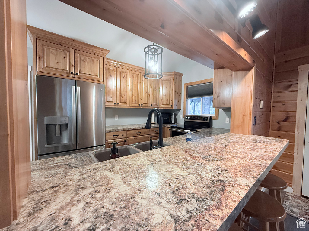 Kitchen with appliances with stainless steel finishes, a sink, a breakfast bar area, a peninsula, and light stone countertops
