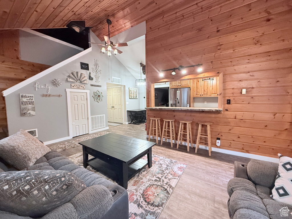 Living area with vaulted ceiling, ceiling fan, wooden ceiling, wood walls, and baseboards