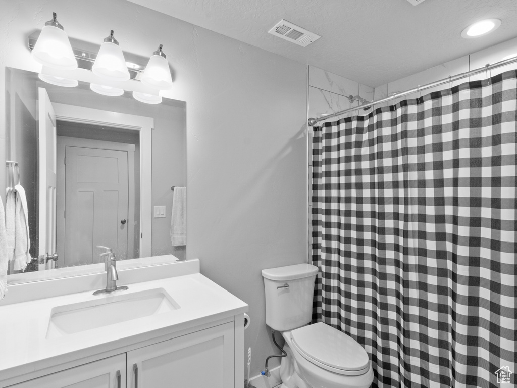 Bathroom featuring toilet, vanity, and curtained shower