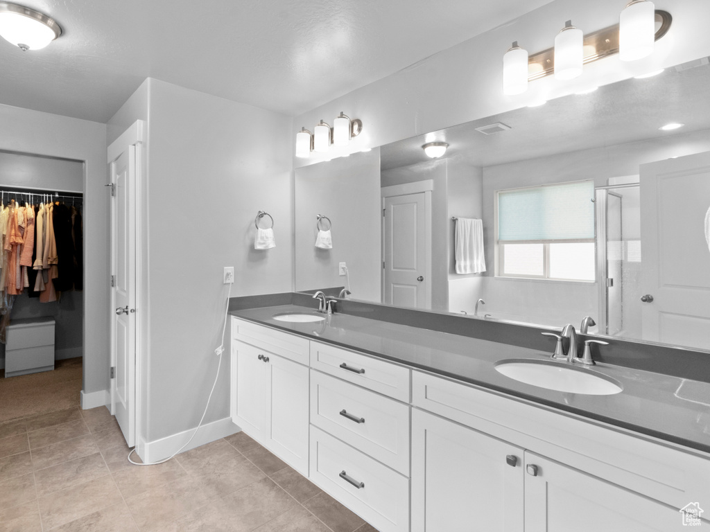 Bathroom with double vanity, baseboards, a walk in closet, tile patterned floors, and a shower with door