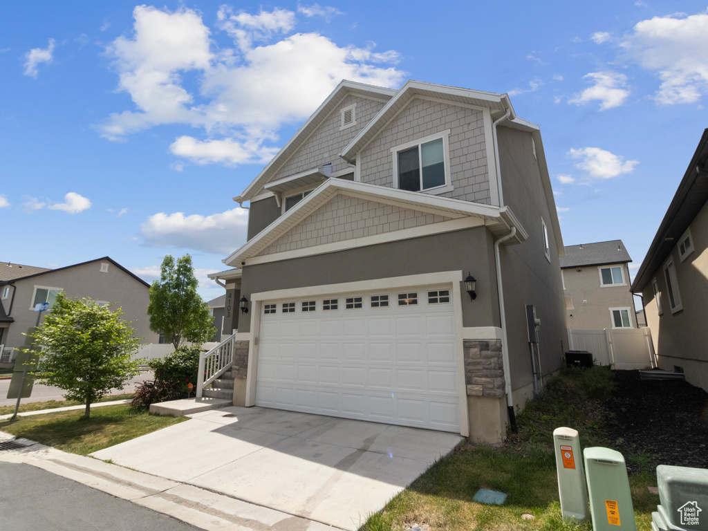 View of front of home featuring driveway, a garage, stone siding, stucco siding, and fence