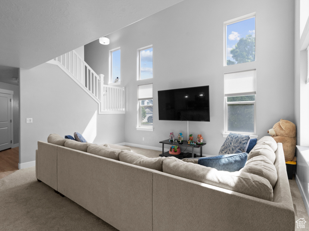 Carpeted living room featuring stairway, baseboards, and a towering ceiling