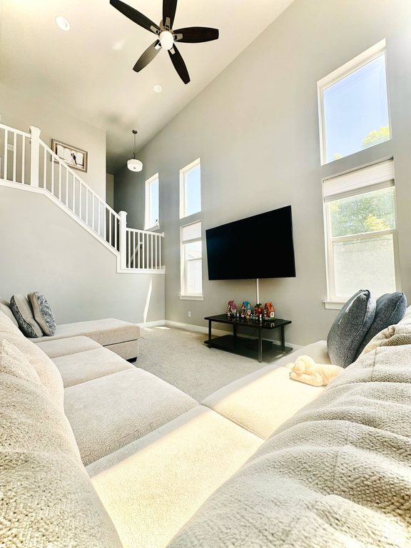 Living room featuring high vaulted ceiling, carpet, stairway, a ceiling fan, and baseboards