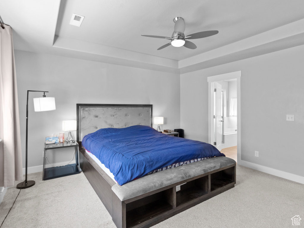Carpeted bedroom with a raised ceiling, baseboards, ensuite bath, and ceiling fan