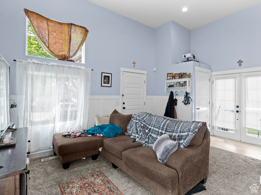 Living room featuring wainscoting, healthy amount of natural light, a towering ceiling, carpet, and french doors