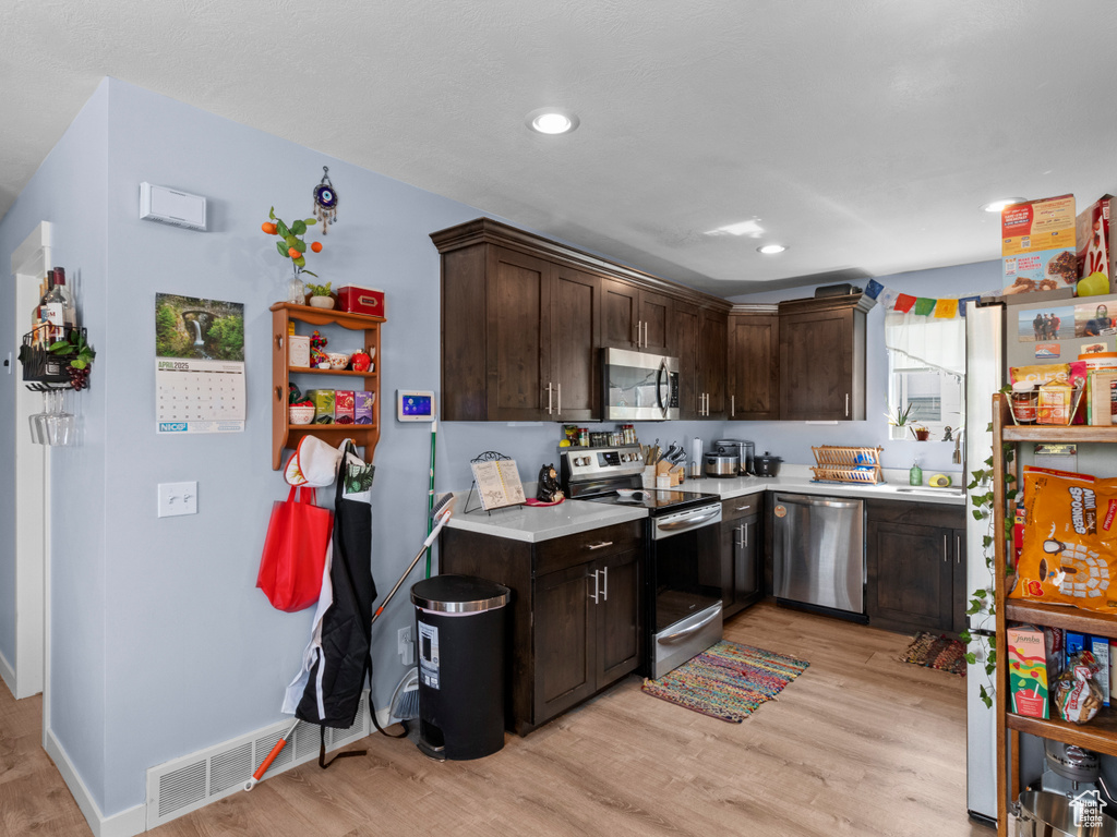 Kitchen with stainless steel appliances, light wood-style flooring, light countertops, dark brown cabinetry, and baseboards