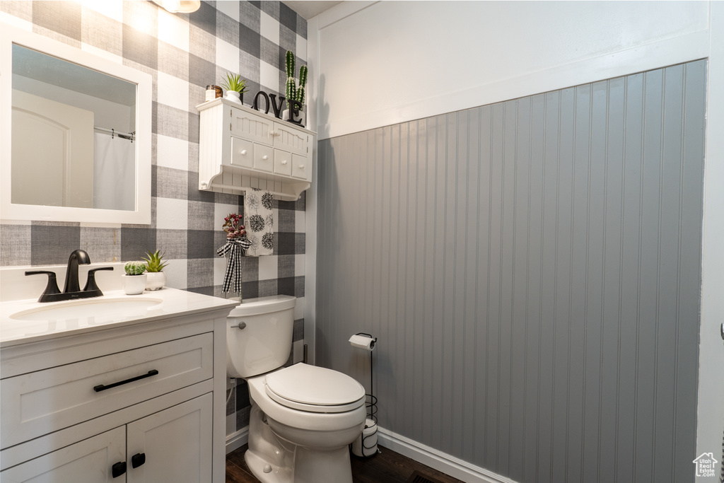 Full bathroom featuring vanity, toilet, wallpapered walls, wood finished floors, and wainscoting