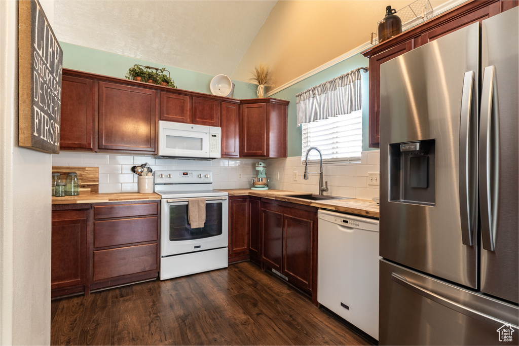 Kitchen featuring white appliances, a sink, vaulted ceiling, wooden counters, and decorative backsplash