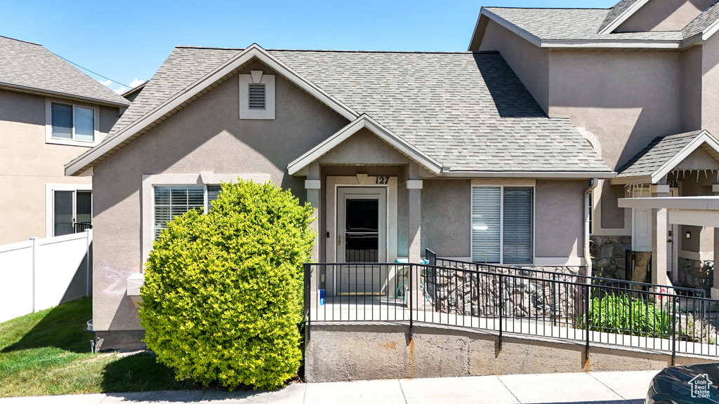 View of front facade featuring stucco siding, fence, and roof with shingles