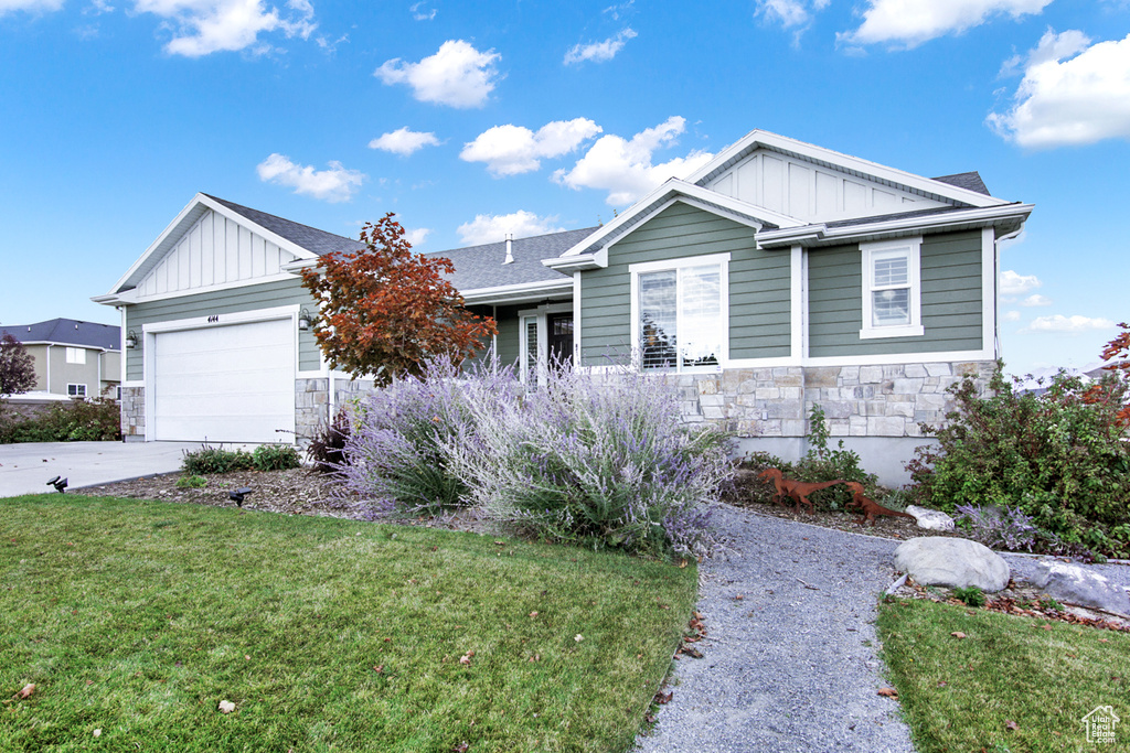View of front of property featuring board and batten siding, stone siding, a front lawn, and concrete driveway