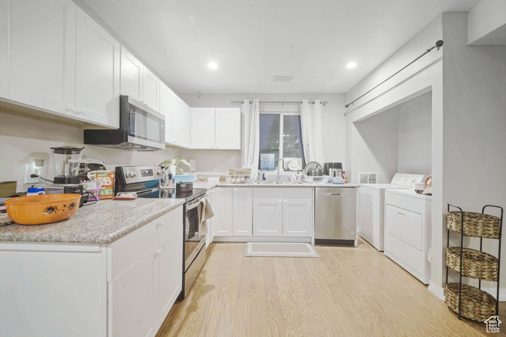 Kitchen with appliances with stainless steel finishes, light wood finished floors, washing machine and clothes dryer, white cabinets, and a sink