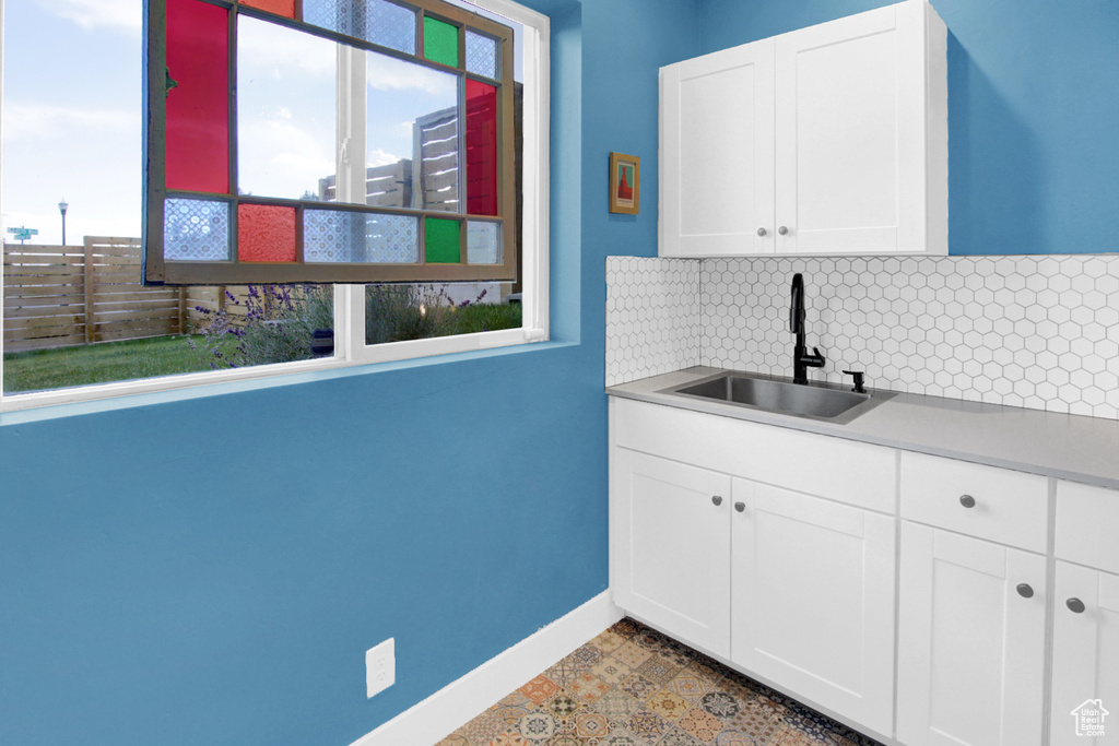 Kitchen with a sink, tasteful backsplash, baseboards, light countertops, and white cabinets