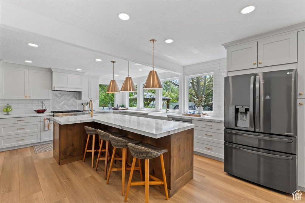 Kitchen featuring stainless steel appliances, tasteful backsplash, light stone countertops, light wood finished floors, and recessed lighting