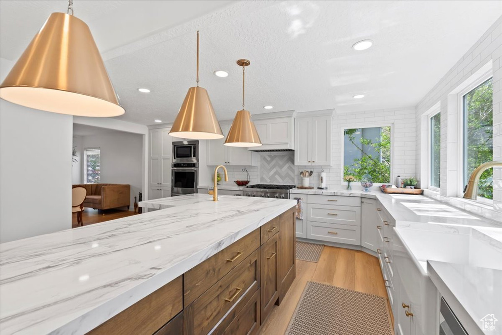 Kitchen with appliances with stainless steel finishes, healthy amount of natural light, light stone counters, recessed lighting, and light wood-style flooring